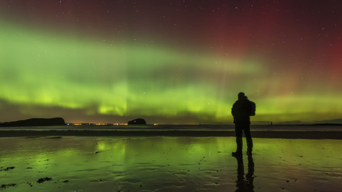 Schottland, East Lothian, Silhouette eines Mannes, der am Seacliff Beach steht und Nordlichter beobachtet, lizenzfreies Stockfoto