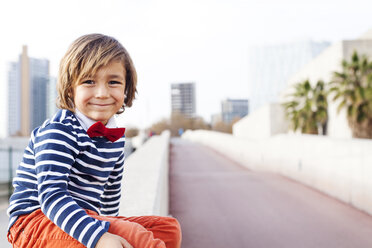 Spanien, Barcelona, Porträt eines fröhlichen kleinen Jungen mit Fliege, der an einer Wand sitzt - VABF000315