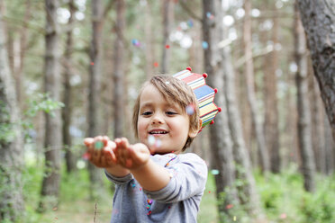 Portrait of smiling little boy wearing paper crown catching confetti - VABF000335