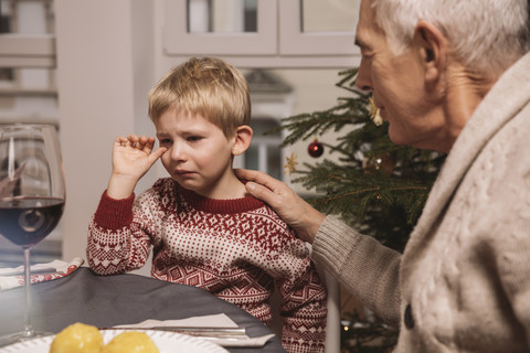 Großvater tröstet traurigen Jungen beim Weihnachtsessen, lizenzfreies Stockfoto