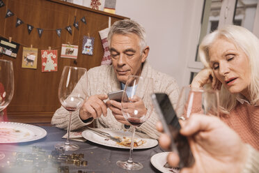 Annoyed senior woman with husband using smartphone after Christmas dinner - MFF002857