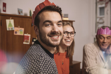 Lächelnder Mann mit Papierkrone und Familie im Hintergrund - MFF002861