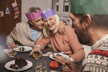 Happy senior couple with paper crowns having Christmas pudding - MFF002868