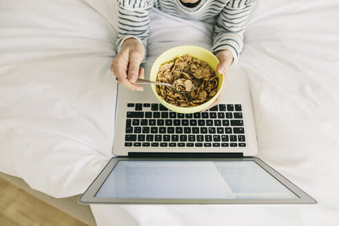 Frau im Bett mit Laptop und Müslischale - EBSF001238