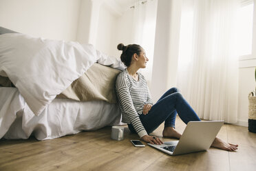 Entspannte Frau sitzt im Schlafzimmer und benutzt einen Laptop - EBSF001240