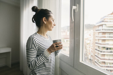 Woman holding cup of coffee looking out of window - EBSF001242