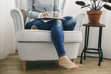 Woman sitting in armchair writing on notepad - EBSF001244