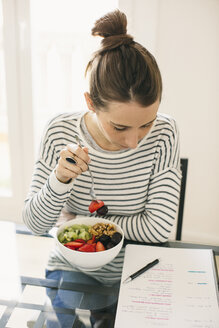Woman sitting at table with fruit muesli looking at notepad - EBSF001249