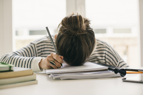 Woman writing on notepad resting her head on table stock photo