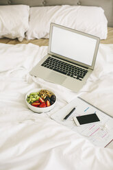 Laptop, notepad, fruit bowl and smartphone with earphones on blanket - EBSF001261