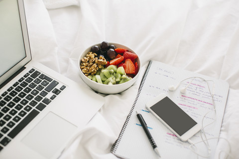 Laptop, notepad, fruit bowl and smartphone with earphones on blanket stock photo