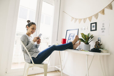 Woman at home laying feet on table looking at cell phone - EBSF001277