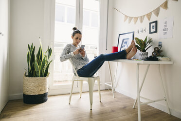 Woman at home laying feet on table looking at cell phone - EBSF001278