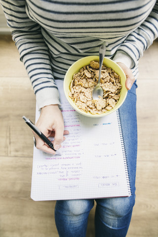 Woman sitting on floor with muesli bowl writing on notepad stock photo