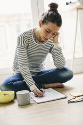 Woman sitting on floor with muesli bowl writing on notepad - EBSF001286