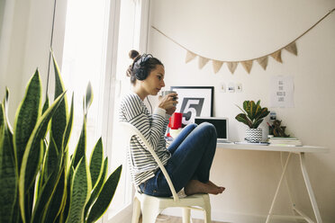 Woman at home sitting at table wearing headphones - EBSF001287