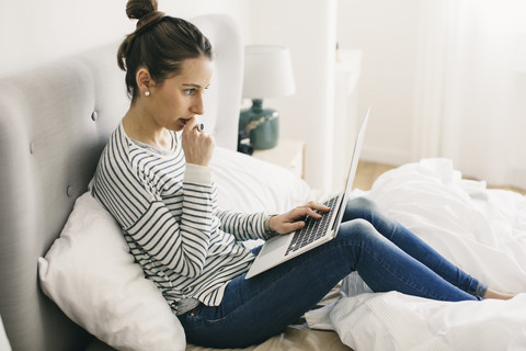 Frau sitzt im Bett und benutzt einen Laptop, lizenzfreies Stockfoto