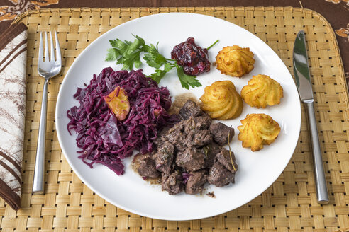 Wildschweingulasch mit Rotkohl, Kroketten, Preiselbeeren und Petersilie auf Teller - PVCF000811