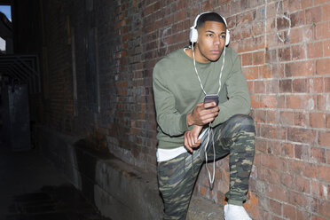 Young man listening music at brick wall at night - BOYF000164