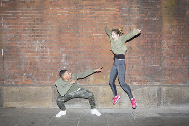 Playful young couple in front of brick wall at night - BOYF000166