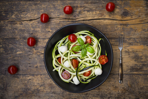 Schüssel mit Zucchini-Spaghetti mit Mozzarella, Kirschtomaten und Basilikum auf Holz - LVF004639