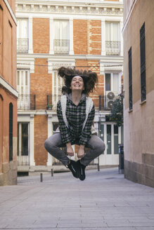 Spanien, Madrid, fröhliche junge Frau, die auf einer Straße in die Luft springt - ABZF000288