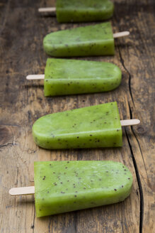 Row of homemade kiwi ice lollies on dark wood - LVF004644