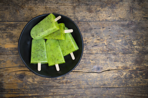 Bowl of homemade kiwi ice lollies on dark wood - LVF004645