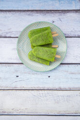 Plate of homemade kiwi ice lollies on wood - LVF004646