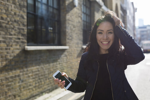 Porträt einer glücklichen jungen Frau mit Mobiltelefon auf einer städtischen Straße - BOYF000180