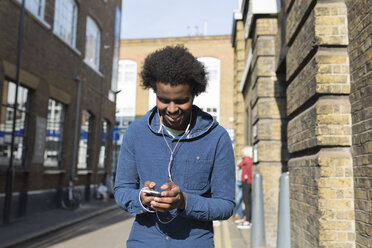 Young man listening to music from cell phone on urban street - BOYF000187
