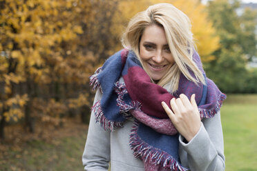 Porträt einer glücklichen jungen Frau mit modischem Schal in einem herbstlichen Park - LFOF000190
