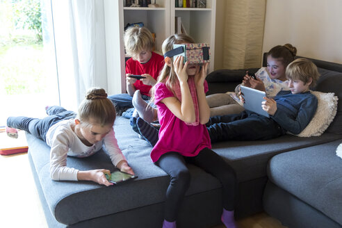 Fünf Kinder auf einer Couch, die verschiedene digitale Geräte benutzen - SARF002643