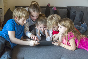 Fünf Kinder auf einer Couch, die gemeinsam ein digitales Tablet benutzen - SARF002646