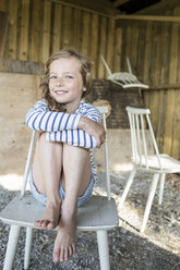 Portrait of smiling blond girl sitting on a wooden chair - OJF000116