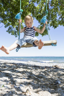 Porträt eines blonden Jungen, der auf einer Schaukel am Strand sitzt - OJF000127