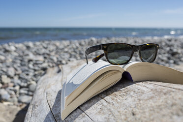Sunglasses on opened book on pebble beach, close-up - OJF000130
