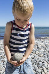 Porträt eines blonden Jungen, der einen Stein am Strand trägt - OJF000133