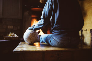 Mann vor dem Kamin sitzend mit einem Fußball - GEMF000791