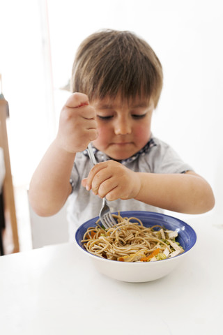 Kleiner Junge isst vegetarische Nudeln mit einer Gabel, lizenzfreies Stockfoto