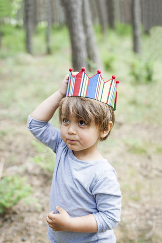 Porträt eines kleinen Jungen mit Holzstock und Papierkrone im Wald, lizenzfreies Stockfoto