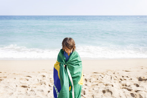 Kleiner Junge in brasilianische Flagge eingewickelt an einem Strand, lizenzfreies Stockfoto