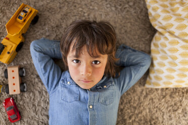 Porträt eines kleinen Jungen auf dem Teppich liegend mit Spielzeugautos neben ihm - VABF000369