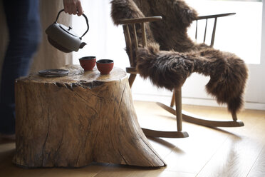 Woman's hand pouring tea into tea bowls in an individual living room - SABF000060