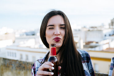 Spanien, Jerez de la Frontera, Porträt einer augenzwinkernden jungen Frau mit einer Bierflasche im Mund - KIJF000241