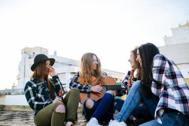 Woman playing a guitar on a roof terrace while her friends listening - KIJF000242