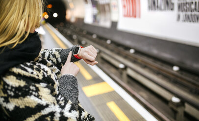 Junge Frau schaut auf ihre Smartwatch beim Warten auf die U-Bahn - MGOF001540