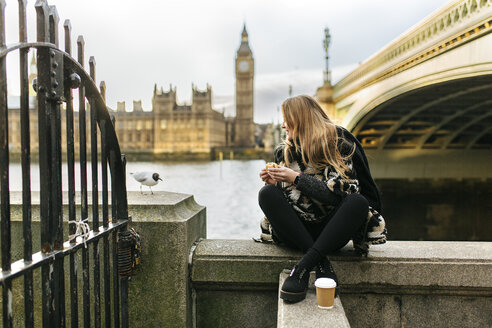 UK, London, young woman taking a snack near Westminster Bridge - MGOF001557