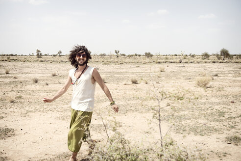 Lächelnder Mann mit Sonnenbrille, der allein in der Wüste spazieren geht - BMAF000116