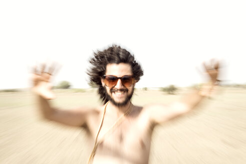 Bare chested man with sunglasses reaching out in desert - BMAF000147